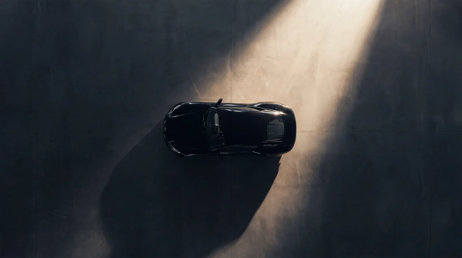 Vista aérea cenital de un coupé negro solo sobre una vasta explanada de concreto oscuro.