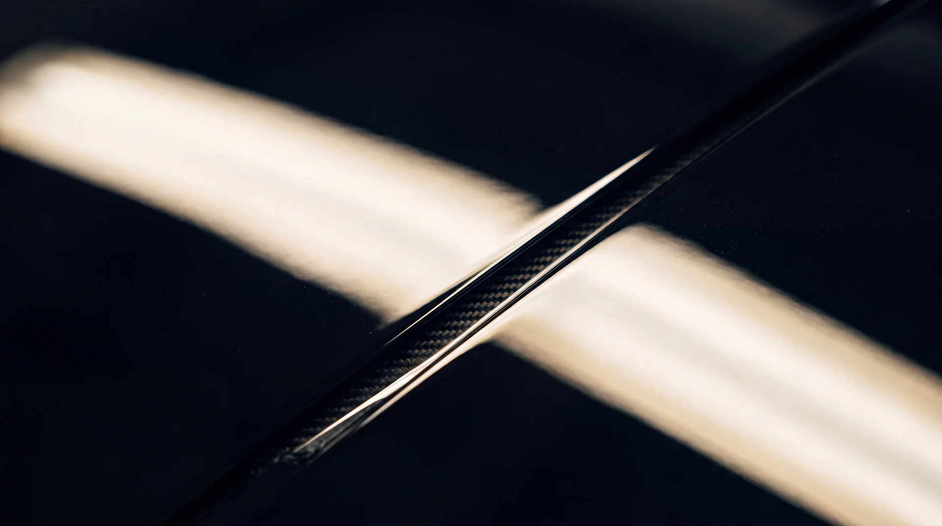 Primer plano extremo de la carrocería negra de un auto bajo una banda de luz en movimiento.